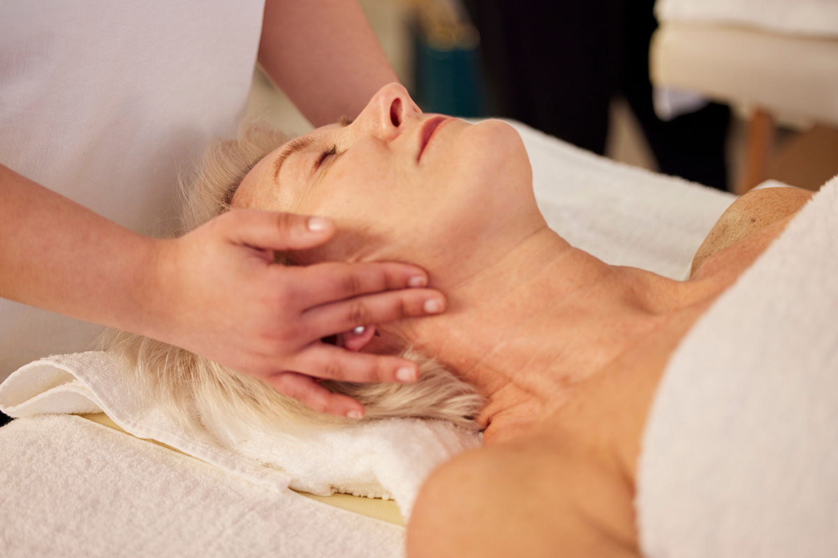 A close-up of a woman receiving a relaxing facial massage at a spa, with the hands of the therapist gently pressing on her temples