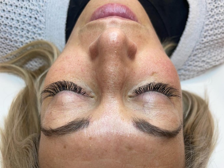 Close-up of a woman lying down with fresh eyelash extensions, showcasing full and defined lashes that enhance her closed eyes, with a relaxed expression on her face.